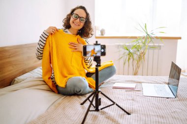 Moda blogcusu, sarı süveter giyen kamera ile vlog için yeni içerik kaydediyor. Modern etkili, modaya uygun bir kadın. Çevrimiçi pazarlama ve satış.