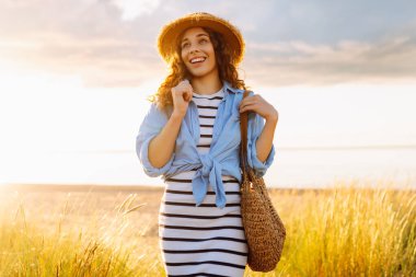 A young woman in a straw hat strolls along the beach on a sunny day. A beautiful woman relaxes and enjoys the sunset. Concept of relaxation and enjoyment. Lifestyle.