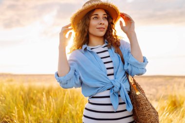 A young woman in a straw hat strolls along the beach on a sunny day. A beautiful woman relaxes and enjoys the sunset. Concept of relaxation and enjoyment. Lifestyle.