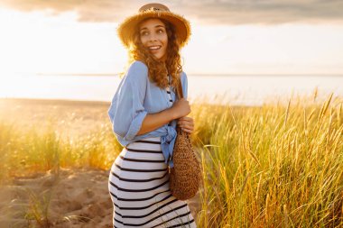 A young woman in a straw hat strolls along the beach on a sunny day. A beautiful woman relaxes and enjoys the sunset. Concept of relaxation and enjoyment. Lifestyle.