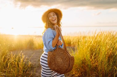 A young woman in a straw hat strolls along the beach on a sunny day. A beautiful woman relaxes and enjoys the sunset. Concept of relaxation and enjoyment. Lifestyle.