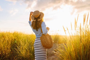 A young woman in a straw hat strolls along the beach on a sunny day. A beautiful woman relaxes and enjoys the sunset. Concept of relaxation and enjoyment. Lifestyle.