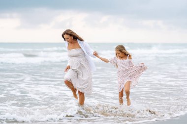 Genç hamile bir kadın kumsalda kızına sarılıyor. Güzel bir kadın ve çocuğu kumlu bir sahilde birlikte vakit geçiriyorlar. Konsept aile, çocukluk ve eğlence hakkındadır..