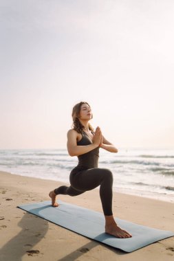 Atletizmde güzel bir kadın güneş ışınlarında kumsalda egzersiz yapar. Atletik bir kadın yoga minderi üzerinde meditasyon yapar, rahatlamış hisseder. Egzersiz, sakinlik ve vücut bakımı kavramları.