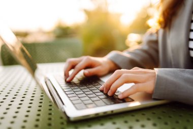 Gün batımında oturan genç bir kadının dizüstü bilgisayarına yazdığı yakın çekim. Dişi bir serbest yazar dizüstü bilgisayarda çalışır ve çatı terasından gün batımına hayran kalır. Uzaktan çalışma kavramı, rahatlama.