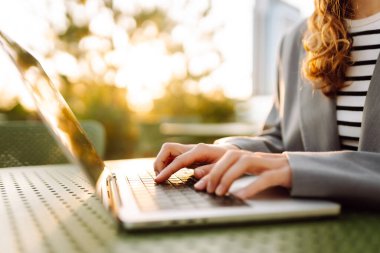 Gün batımında oturan genç bir kadının dizüstü bilgisayarına yazdığı yakın çekim. Dişi bir serbest yazar dizüstü bilgisayarda çalışır ve çatı terasından gün batımına hayran kalır. Uzaktan çalışma kavramı, rahatlama.