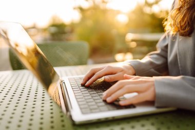 Gün batımında oturan genç bir kadının dizüstü bilgisayarına yazdığı yakın çekim. Dişi bir serbest yazar dizüstü bilgisayarda çalışır ve çatı terasından gün batımına hayran kalır. Uzaktan çalışma kavramı, rahatlama.