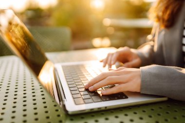 Gün batımında oturan genç bir kadının dizüstü bilgisayarına yazdığı yakın çekim. Dişi bir serbest yazar dizüstü bilgisayarda çalışır ve çatı terasından gün batımına hayran kalır. Uzaktan çalışma kavramı, rahatlama.