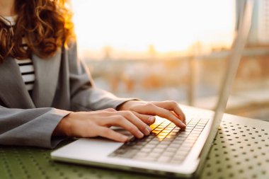 Gün batımında oturan genç bir kadının dizüstü bilgisayarına yazdığı yakın çekim. Dişi bir serbest yazar dizüstü bilgisayarda çalışır ve çatı terasından gün batımına hayran kalır. Uzaktan çalışma kavramı, rahatlama.