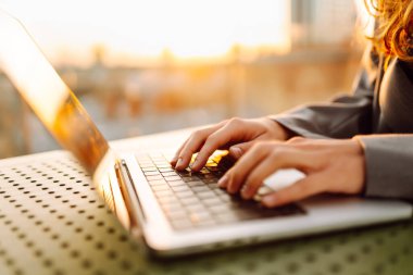 Gün batımında oturan genç bir kadının dizüstü bilgisayarına yazdığı yakın çekim. Dişi bir serbest yazar dizüstü bilgisayarda çalışır ve çatı terasından gün batımına hayran kalır. Uzaktan çalışma kavramı, rahatlama.