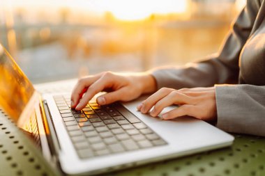 Gün batımında oturan genç bir kadının dizüstü bilgisayarına yazdığı yakın çekim. Dişi bir serbest yazar dizüstü bilgisayarda çalışır ve çatı terasından gün batımına hayran kalır. Uzaktan çalışma kavramı, rahatlama.