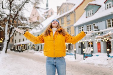 Şehrin sokaklarında karda eğlenen mutlu bir kadının portresi. Parlak ceketli güzel bir turist şehrin sokaklarında kış gününün tadını çıkarıyor. Turizm ve eğlence kavramı.