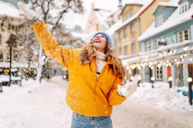 Şehrin sokaklarında karda eğlenen mutlu bir kadının portresi. Parlak ceketli güzel bir turist şehrin sokaklarında kış gününün tadını çıkarıyor. Turizm ve eğlence kavramı.