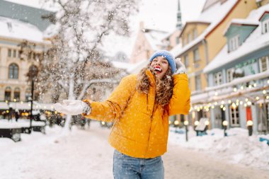 Şehrin sokaklarında karda eğlenen mutlu bir kadının portresi. Parlak ceketli güzel bir turist şehrin sokaklarında kış gününün tadını çıkarıyor. Turizm ve eğlence kavramı.
