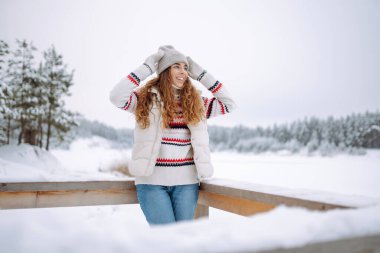 Neşeli bir kadın gölün yakınındaki karlı manzaranın tadını çıkarıyor. Güzel bir kadın kış günü dışarıda eğleniyor. Seyahat, yürüyüş ve mevsimlik kavramları.