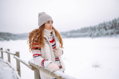 Neşeli bir kadın gölün yakınındaki karlı manzaranın tadını çıkarıyor. Güzel bir kadın kış günü dışarıda eğleniyor. Seyahat, yürüyüş ve mevsimlik kavramları.