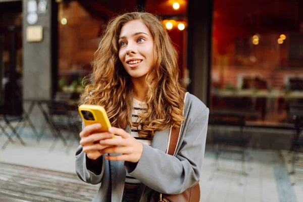 Şık giyinmiş genç bir kadın telefonuyla şehirde dolaşmaktan hoşlanıyor. Güneşli bir günde güzel bir kadın telefonuyla mesaj atıyor. Konsept: blog yazma, moda, yaşam tarzı.