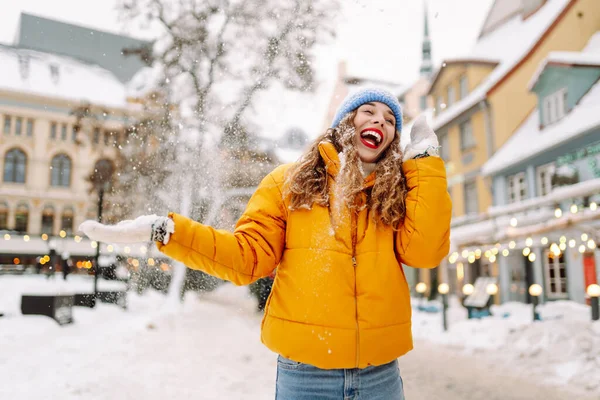 Şehrin sokaklarında karda eğlenen mutlu bir kadının portresi. Parlak ceketli güzel bir turist şehrin sokaklarında kış gününün tadını çıkarıyor. Turizm ve eğlence kavramı.