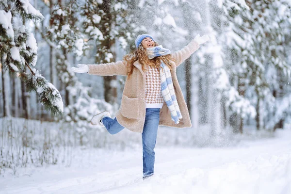 Sıcak kış kıyafetleri içinde neşeli bir kadın güneşli bir ormanda karla eğlenir. Güzel bir kadın dışarıda kış gününün tadını çıkarır. Eğlence anlayışı, doğa. Etkin yaşam biçimi.