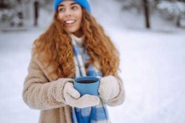 Termoslu genç bir kadın karlı bir ormanda bir kütüğün üzerinde oturuyor. Neşeli bir kadın güneşli bir günde kışın tadını çıkarır. Konsept: İçkiler, doğa, macera.