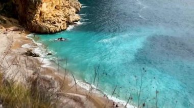 Dalgalar yumuşak kumla kaplı ve kayalıklarla çevrili huzurlu bir plaja nazikçe çarpar. Berrak mavi su güneşli bir günde dinlenmeye ve keşfe davet eder..