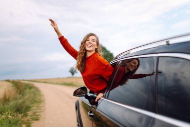 Neşeli kadın güneşli bir günde kendini özgür hissederek arabanın camından sarkıyor. Yolculukta olan genç bir kadın pencereden dışarı bakar ve esintiyi yakalar. Araba macerası, özgürlük ve rahatlama kavramı.