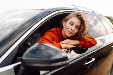 Neşeli kadın güneşli bir günde kendini özgür hissederek arabanın camından sarkıyor. Yolculukta olan genç bir kadın pencereden dışarı bakar ve esintiyi yakalar. Araba macerası, özgürlük ve rahatlama kavramı.