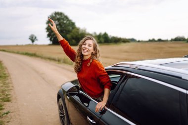 Neşeli kadın güneşli bir günde kendini özgür hissederek arabanın camından sarkıyor. Yolculukta olan genç bir kadın pencereden dışarı bakar ve esintiyi yakalar. Araba macerası, özgürlük ve rahatlama kavramı.