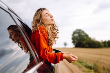 Neşeli kadın güneşli bir günde kendini özgür hissederek arabanın camından sarkıyor. Yolculukta olan genç bir kadın pencereden dışarı bakar ve esintiyi yakalar. Araba macerası, özgürlük ve rahatlama kavramı.