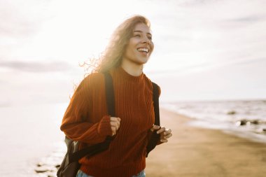Sırt çantalı genç bir kadın kendini özgür hissediyor ve gün batımında deniz manzarasının tadını çıkarıyor. Güzel bir gezgin sahilde geziniyor. Özgürlük ve rahatlama kavramı.