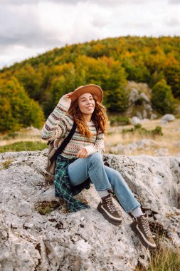 Şapka takan ve sırt çantası taşıyan yürüyüşçü dağlarda yürüyüş yolu boyunca yürür. Güzel bir kadın dağ manzarasından zevk alır ve gün batımında özgür hisseder. Seyahat ve yürüyüş kavramları. Etkin yaşam biçimi.