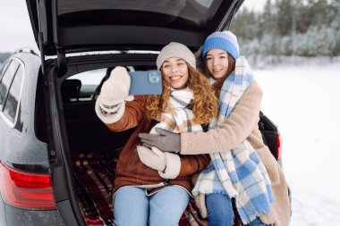 İki genç kadın güneşli kış gününde arabanın bagajında otururken telefonlarıyla selfie çekiyorlar. Güzel arkadaşlar eğleniyor, blog yapıyor, karlı ormanda yolculuğun tadını çıkarıyor. Arkadaşlık kavramı, macera.