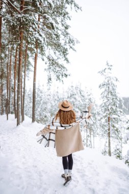 Şapkalı ve fularlı neşeli bir kadın güneşli bir günde karlı bir ormanın tadını çıkarır. Tatlı bir kadın kış günü doğa yürüyüşüne çıkar. Yürüyüş, keyif ve hafta sonu kavramları.