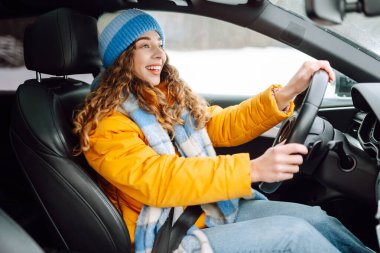 Karlı bir günde parlak sarı ceketli genç bir kadın araba kullanıyor. Güzel bir kadın soğuk bir kış gününde araba sürmekten hoşlanır. Ulaşım kavramı, keyif. Yaşam biçimi.