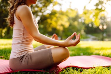 Spor elbiseli güzel bir kadın gün batımında yoga minderinde meditasyon yapıyor. Atletik bir kadın güneşli bir parkta yoga yapıyor ve doğanın tadını çıkarıyor. Yoga kavramları, esneme. Sağlıklı yaşam tarzı.