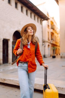 Şapkalı neşeli bayan turist ve telefon ile şehrin caddelerinde sarı valiz gezintileri yapıyor. Telefonu olan genç bir kadın güneşli bir günde blog yazıyor, gezinin tadını çıkarıyor. Bloglar, hafta sonları için kavramlar.