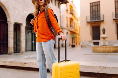 Şapkalı neşeli bayan turist ve telefon ile şehrin caddelerinde sarı valiz gezintileri yapıyor. Telefonu olan genç bir kadın güneşli bir günde blog yazıyor, gezinin tadını çıkarıyor. Bloglar, hafta sonları için kavramlar.