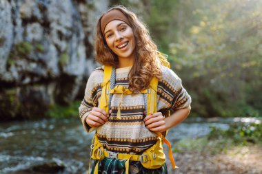 Parlak sırt çantalı bir yürüyüşçü ormandaki yüksek dağ nehri yakınlarında yürüyüş yolu boyunca yürür. Güzel bir kadın güneşli bir günde nehir ve dağ manzarası boyunca yürümekten hoşlanır. Konseptler: doğa, yürüyüş.