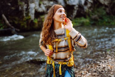 Parlak sırt çantalı bir yürüyüşçü ormandaki yüksek dağ nehri yakınlarında yürüyüş yolu boyunca yürür. Güzel bir kadın güneşli bir günde nehir ve dağ manzarası boyunca yürümekten hoşlanır. Konseptler: doğa, yürüyüş.