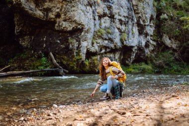 Parlak sırt çantalı bir yürüyüşçü ormandaki yüksek dağ nehri yakınlarında yürüyüş yolu boyunca yürür. Güzel bir kadın güneşli bir günde nehir ve dağ manzarası boyunca yürümekten hoşlanır. Konseptler: doğa, yürüyüş.