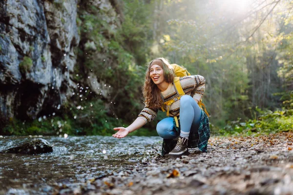 Parlak sırt çantalı bir yürüyüşçü ormandaki yüksek dağ nehri yakınlarında yürüyüş yolu boyunca yürür. Güzel bir kadın güneşli bir günde nehir ve dağ manzarası boyunca yürümekten hoşlanır. Konseptler: doğa, yürüyüş.