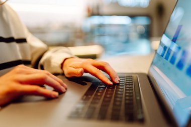 Rahat bir kafede otururken dizüstü bilgisayarda serbest çalışan kadın tipler. Yakın plan. İçerideki bir masada dizüstü bilgisayarda çalışan kadın eller. Uzak çalışma, iş ve öğrenim kavramları.