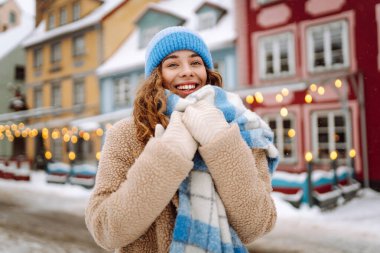 Keyifli kadın portresi rahat giysiler içinde şehrin karlı sokaklarında parlak ışıkların önünde geziniyor. Güzel bir kadın kış gününün tadını çıkarır. Kavram: Turizm, tatil, yaşam tarzı.