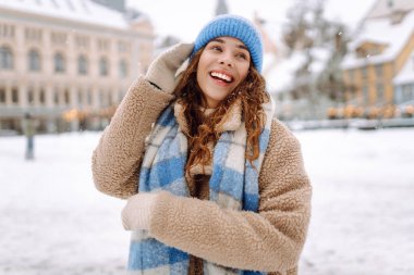 Keyifli kadın portresi rahat giysiler içinde şehrin karlı sokaklarında parlak ışıkların önünde geziniyor. Güzel bir kadın kış gününün tadını çıkarır. Kavram: Turizm, tatil, yaşam tarzı.