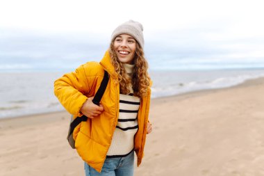 Parlak ceketli bir gezginin portresi arka planda deniz olan ahşap bir yürüyüş yolunda duruyor. Güzel bir kadın deniz manzarasını sever. Seyahat ve doğa kavramları.