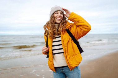 Parlak ceketli bir gezginin portresi arka planda deniz olan ahşap bir yürüyüş yolunda duruyor. Güzel bir kadın deniz manzarasını sever. Seyahat ve doğa kavramları.