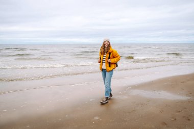 Parlak ceketli bir gezginin portresi arka planda deniz olan ahşap bir yürüyüş yolunda duruyor. Güzel bir kadın deniz manzarasını sever. Seyahat ve doğa kavramları.