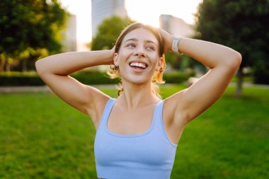 Atletik giysili genç bir kadın parkta güneşli bir günün tadını çıkarıyor. Atletik bir kadın koşudan sonra sevinçten havalara uçar. Spor, keyif ve rahatlama kavramı.