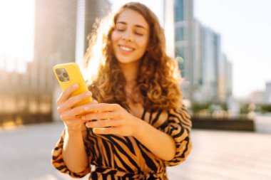 Güneşli bir günde Metropolis 'in arka planına karşı genç bir kadının elindeki parlak renkli telefonun yakın çekimi. Telefon mesajları olan güzel bir kadın, dışarıda geziniyor. Kavram: Turizm, teknoloji.