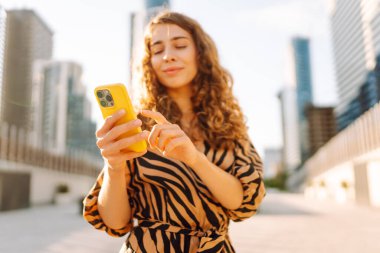 Güneşli bir günde Metropolis 'in arka planına karşı genç bir kadının elindeki parlak renkli telefonun yakın çekimi. Telefon mesajları olan güzel bir kadın, dışarıda geziniyor. Kavram: Turizm, teknoloji.